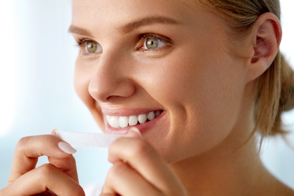 Young woman applying a teeth whitening strip