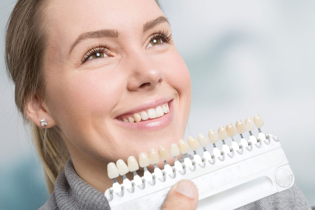 Dentist holding the teeth whitening chart in front of a smiling woman.