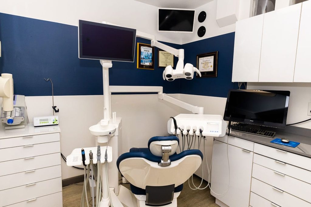 Dental exam room with computer monitors on the wall, a dental chair and other zoom whitening dental equipment.