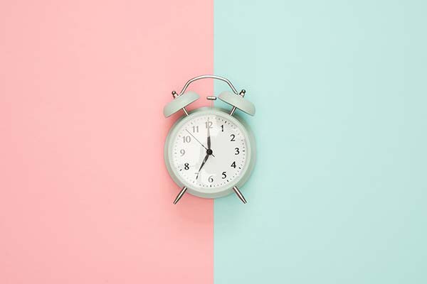 Teal colored alarm clock up against a pink and teal background.
